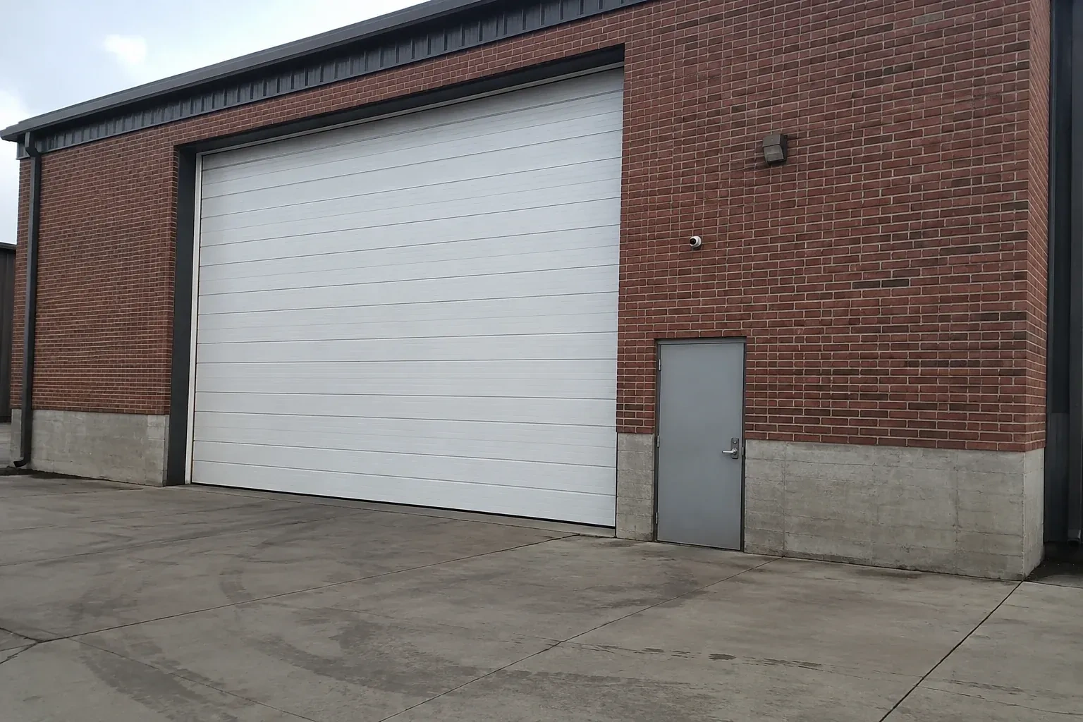Tall closed sectional loading door beside a personnel door at a brick unit. — Commercial Sectional Door Repair, Orillia